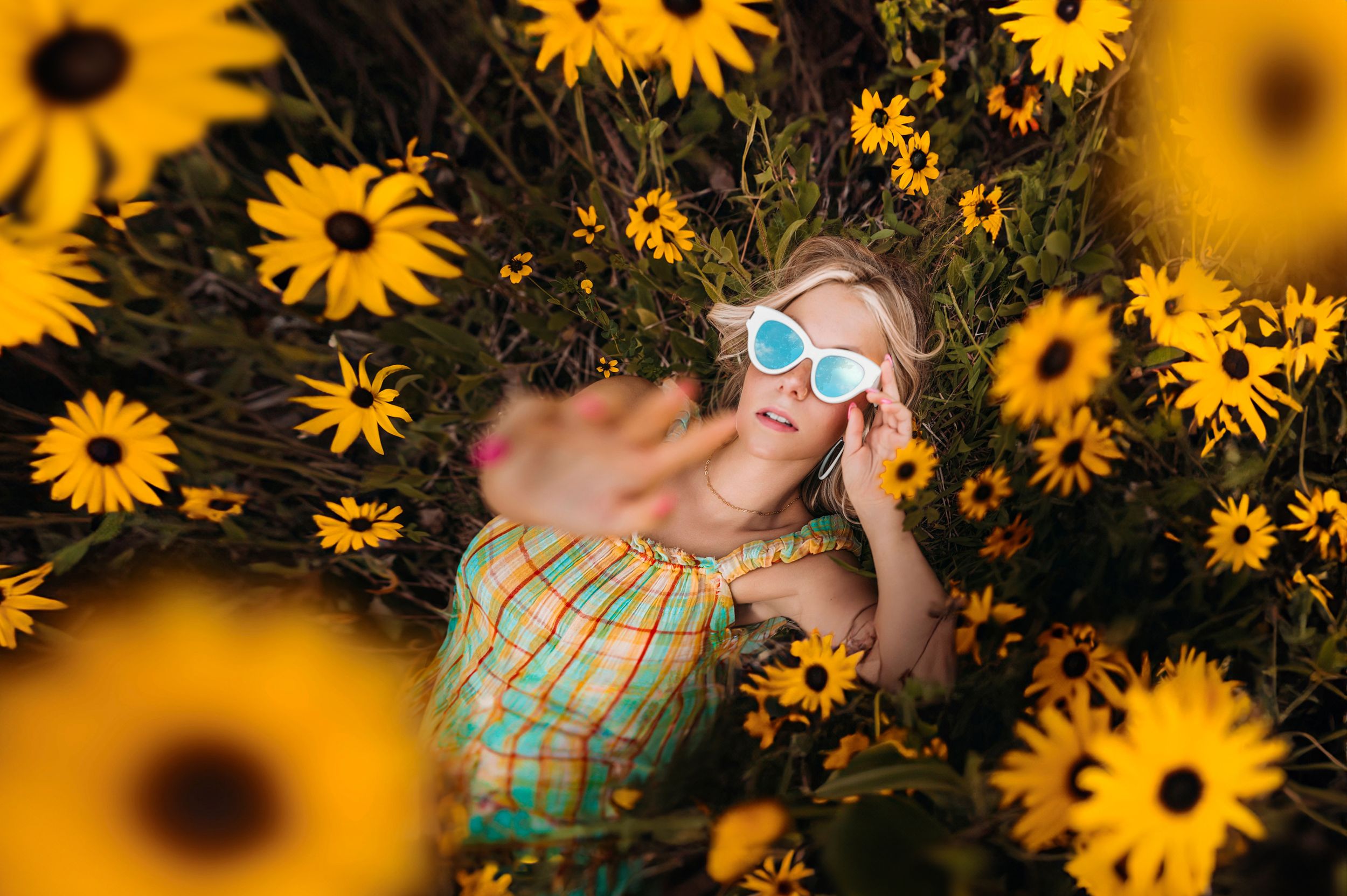 Child lying in field of yellow sunflowers wearing blue heart-shaped sunglasses.