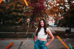 Young woman smiling outdoors with colorful confetti streamers flying around her in an autumn setting.