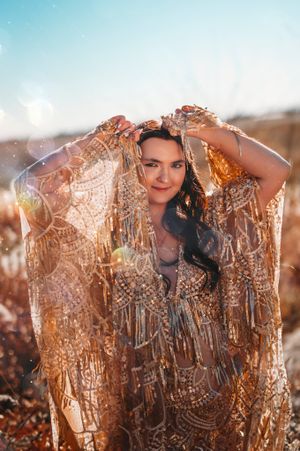 Woman in ornate gold beaded shawl posing outdoors in warm sunlight.