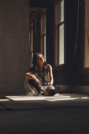 Young woman sitting cross-legged on a floor in natural light streaming through tall windows in an urban building.