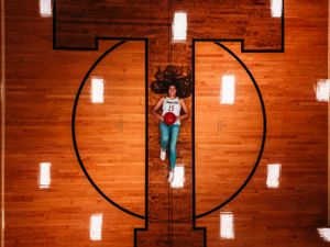 Aerial view of female basketball player lying on hardwood court center circle.