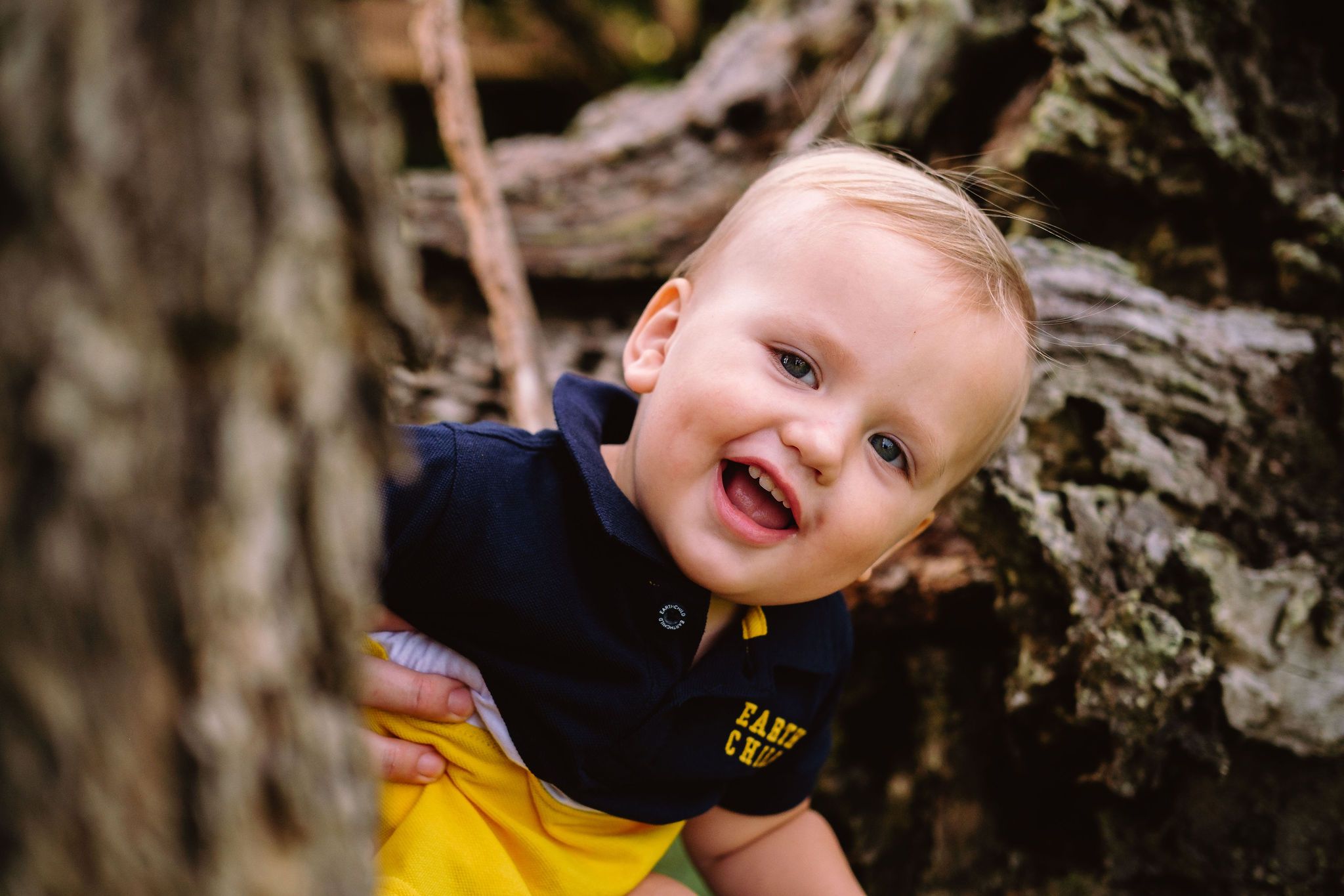 Little boy peeking around a tree and laughing at Kwambonambi