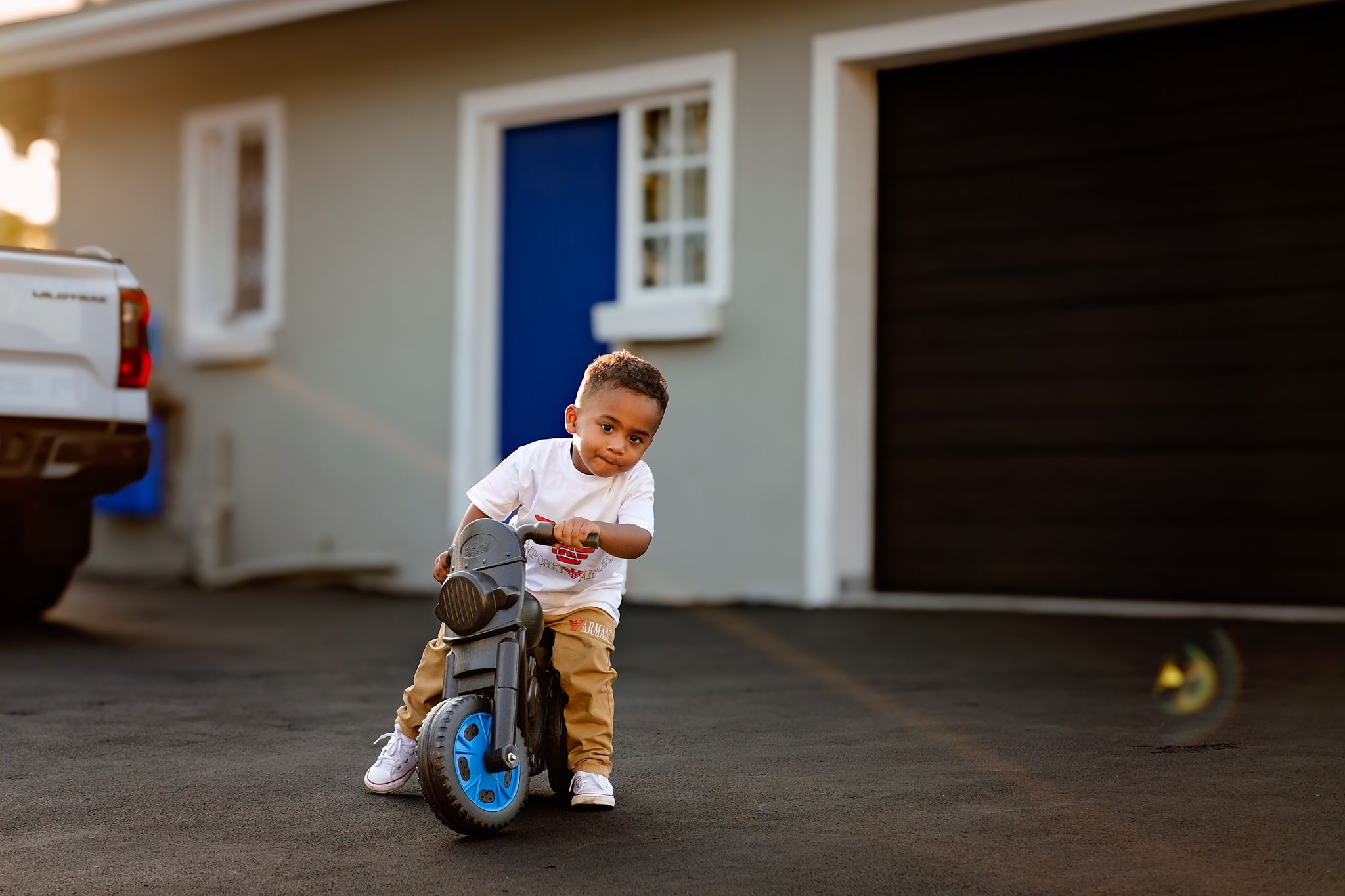 Two-year-old boy riding his motorbike in the family driveway