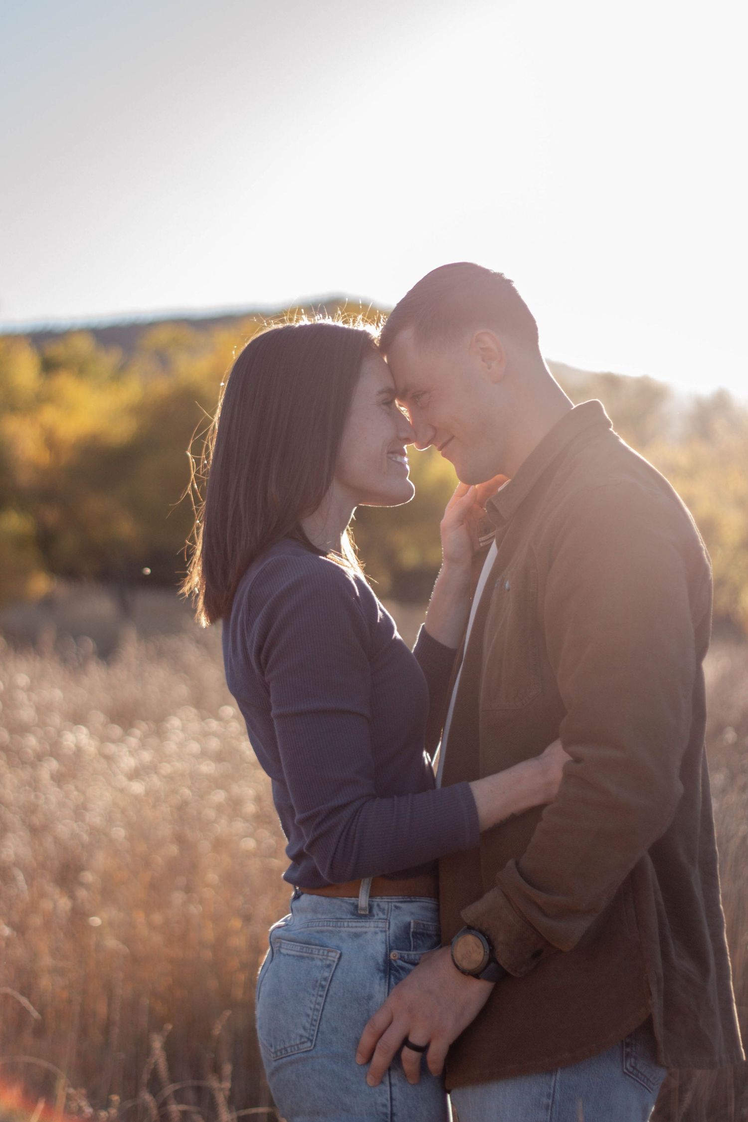 A romantic couple shares an intimate moment in a golden sunlit field during sunset. Engagement photoshoot Colorado in Fall.