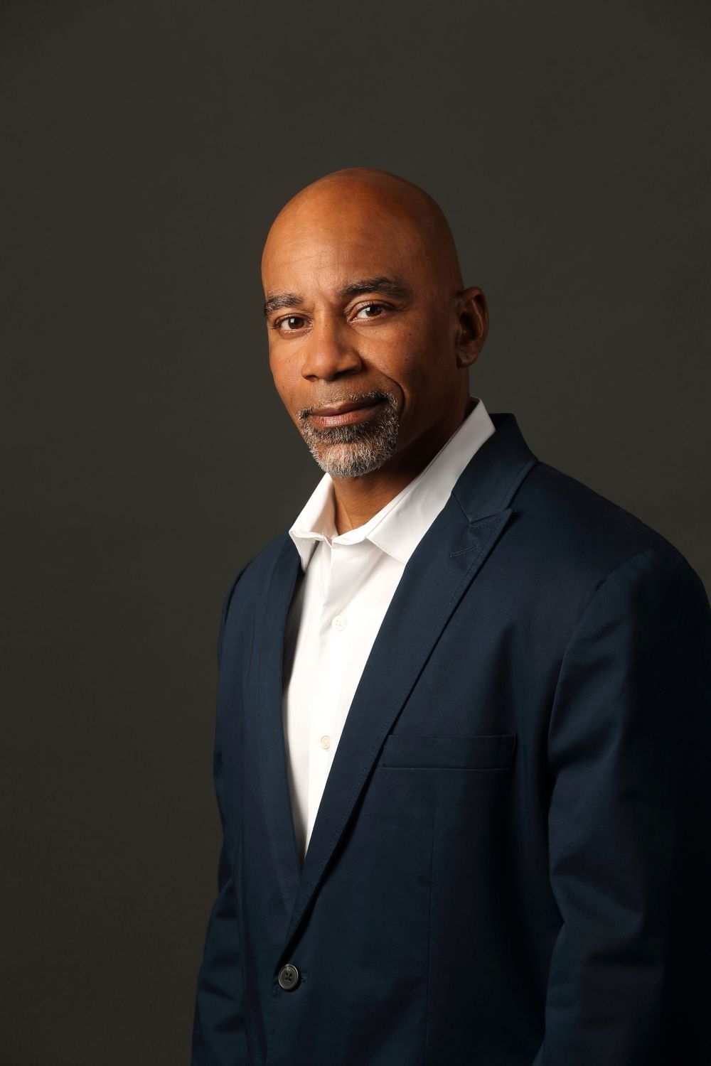 Professional studio portrait of a mature businessman in a navy blazer and white shirt against a dark backdrop.
