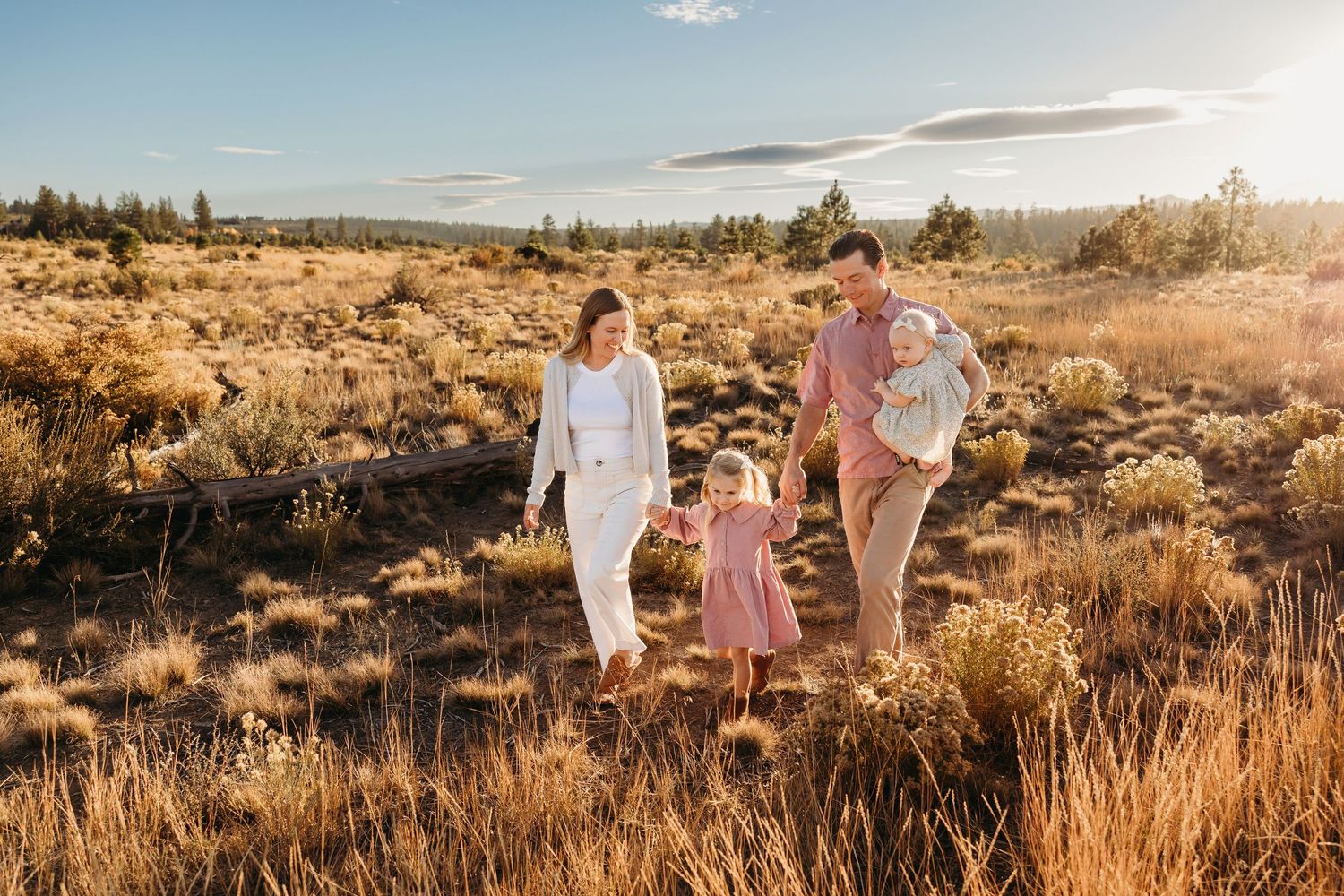 A family walks together along a scenic autumn path beside a serene lake with tall grass and evergreen trees.