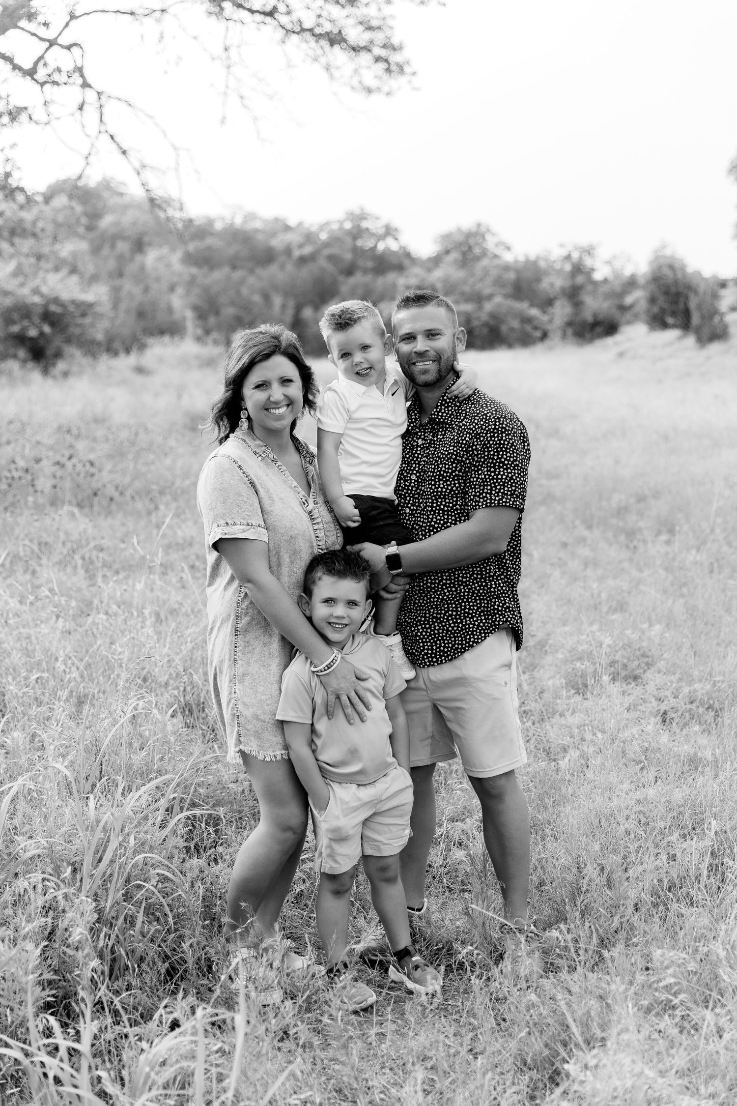 A family of four poses together in a sunny field for a black and white portrait.