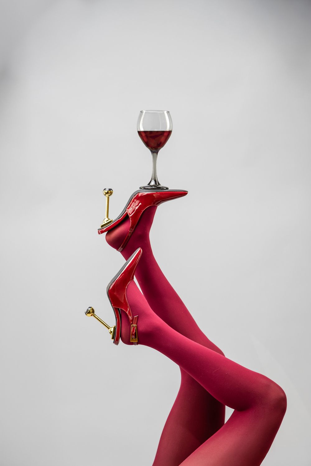 Fashion concept image. Red heels on an upside down feet balancing a glass of red wine
