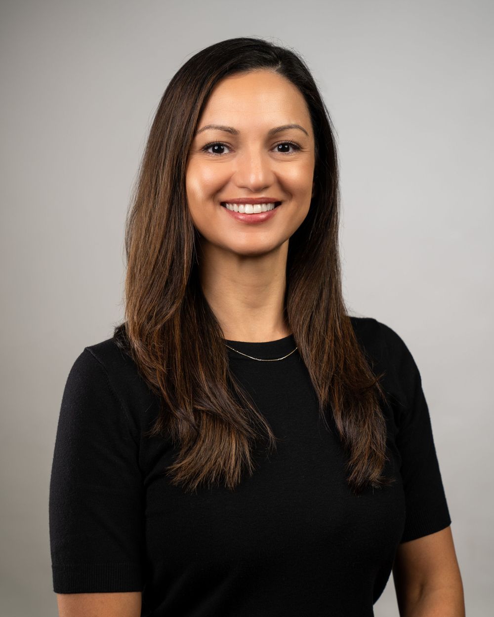 Professional headshot against gray background wearing black top.