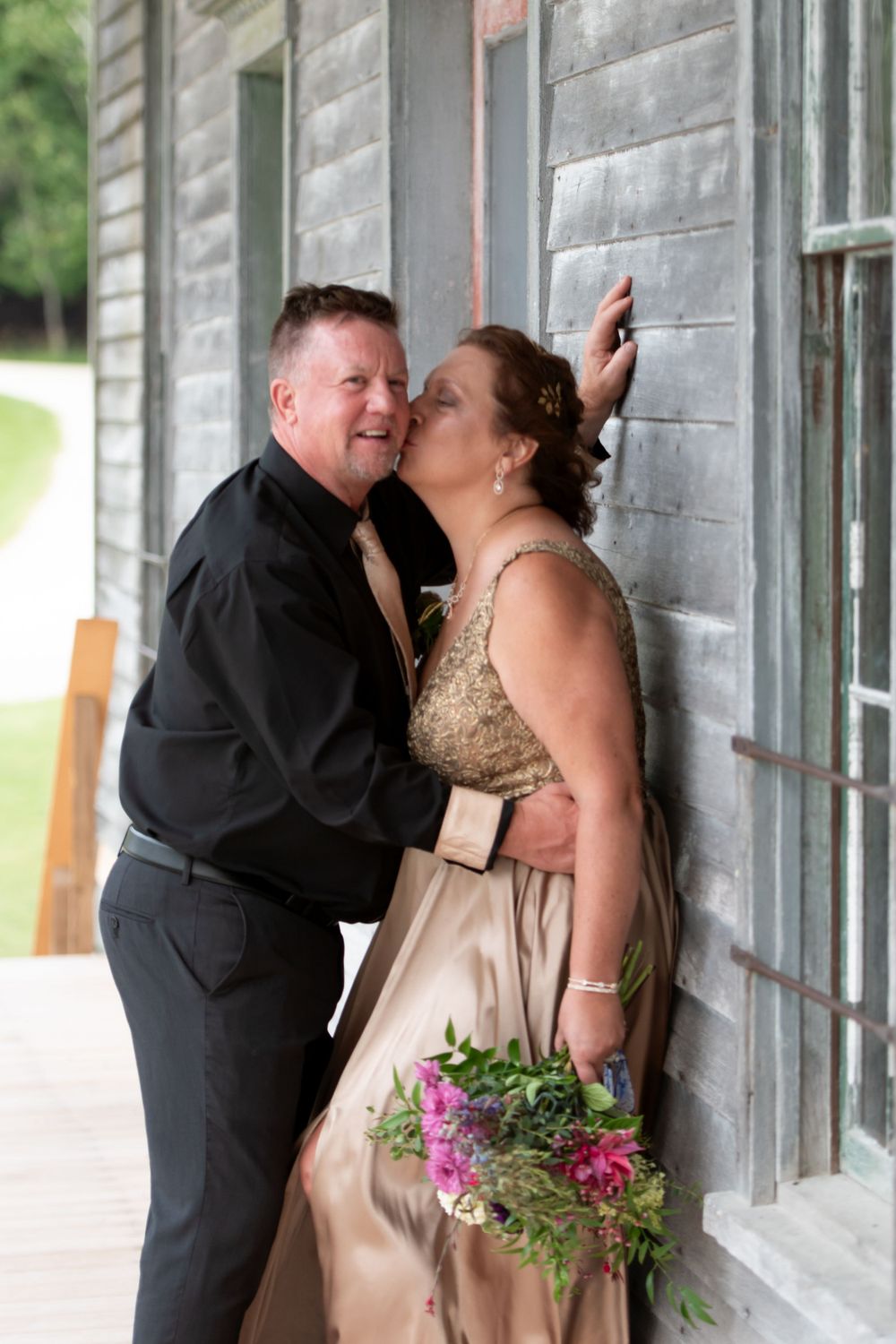 Couple in formal attire sharing romantic moment outside rustic gray building. fayette state park