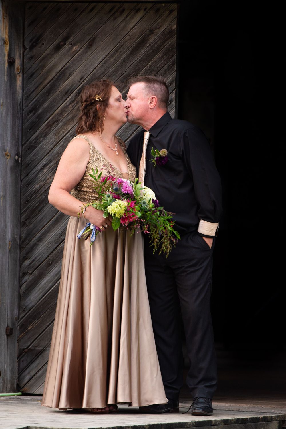 Couple in formal wear with floral bouquet share intimate moment by wooden barn door. fayette state park