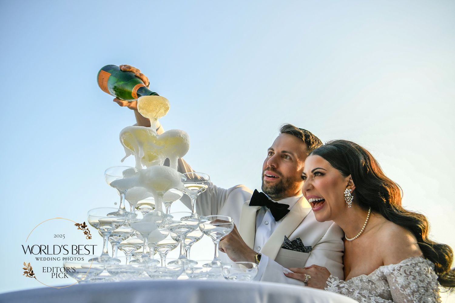 A celebratory moment with champagne being poured into a tower of glasses at an outdoor wedding reception.