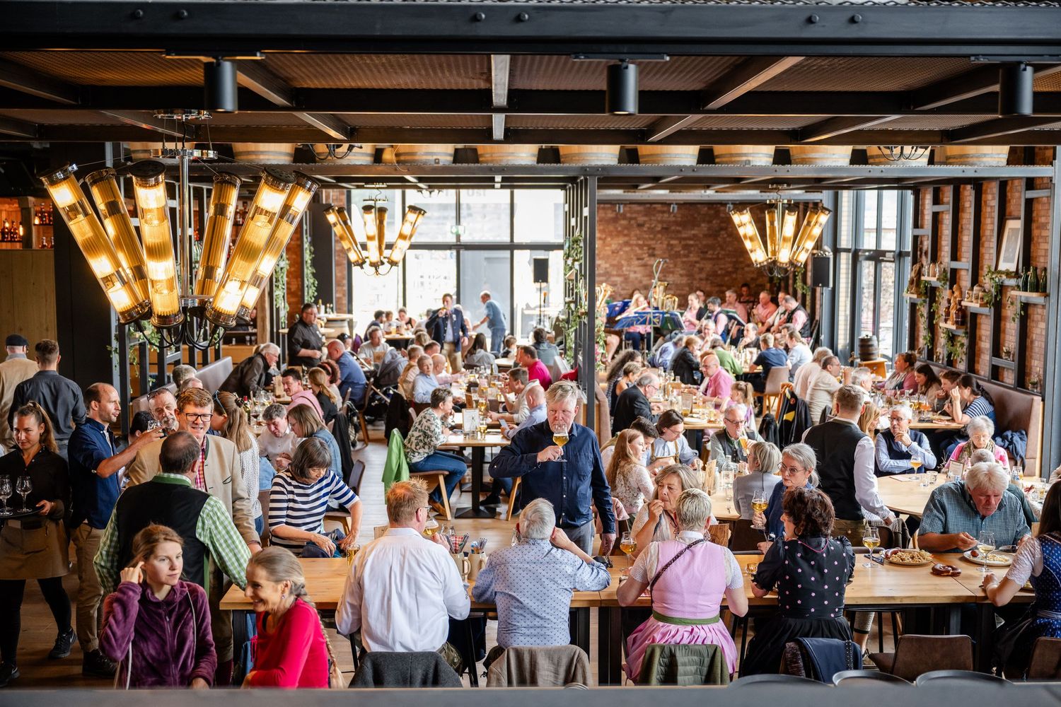 Busy restaurant interior with exposed brick walls and industrial lighting filled with diners at communal tables.