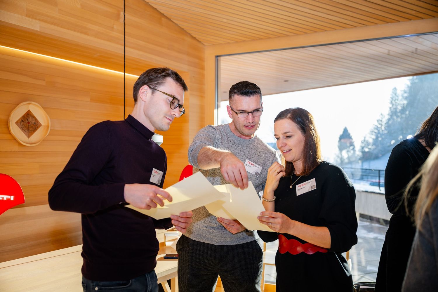 Three colleagues in casual attire review documents together in a modern wood-paneled office space.