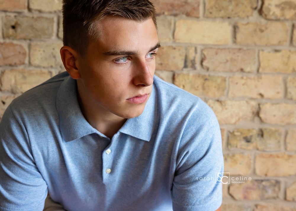 Person in light blue polo shirt looking contemplatively to the side against exposed brick wall background.