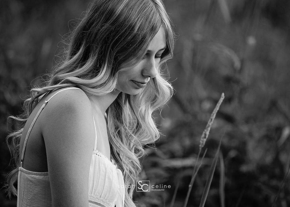 Black and white portrait of a young woman with long wavy hair smiling softly outdoors.