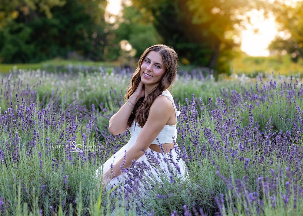 Young woman smiling in a lavender field at golden hour, wearing a white crop top and floral skirt.