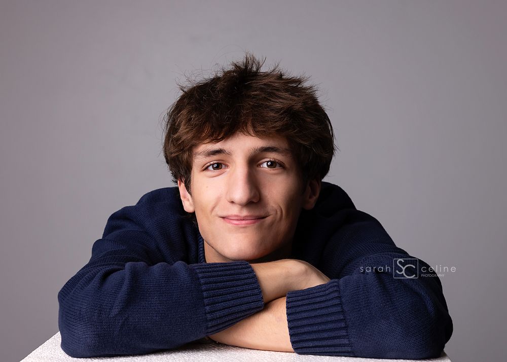 Teen boy in navy hoodie posing with arms crossed, studio senior portrait photography.