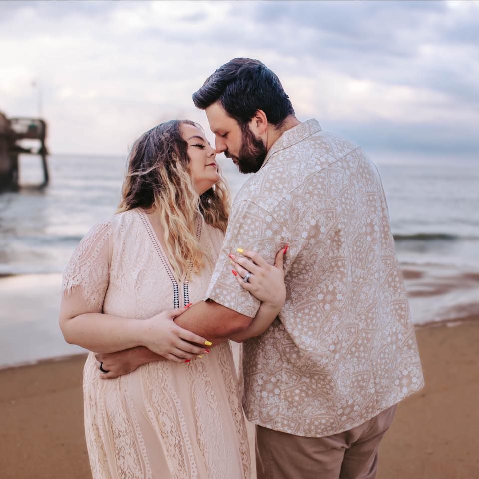 Romantic beach engagement photo of couple in neutral tones embracing at sunset.