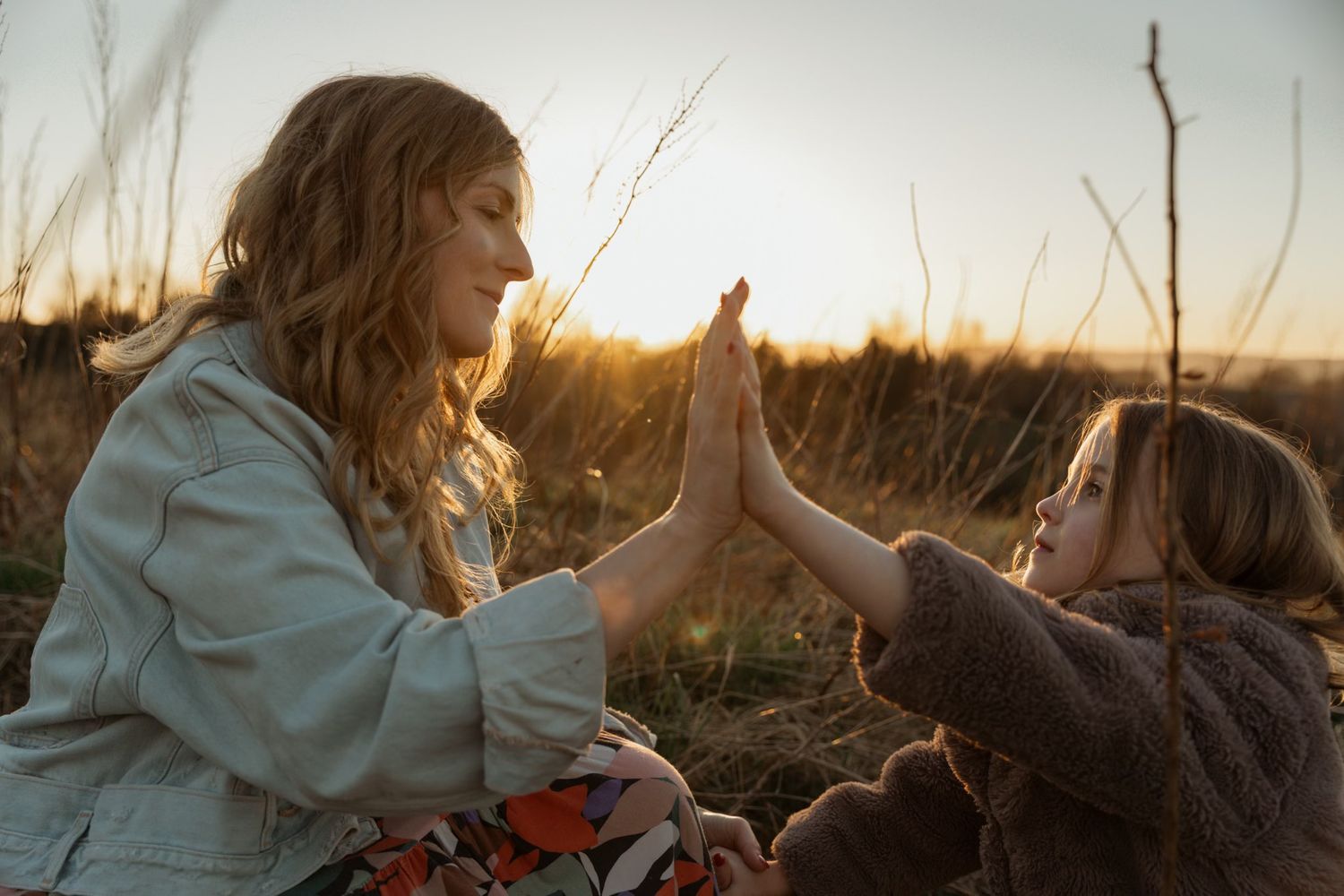 Mother and child touching hands during a quiet moment at sunset in an open field