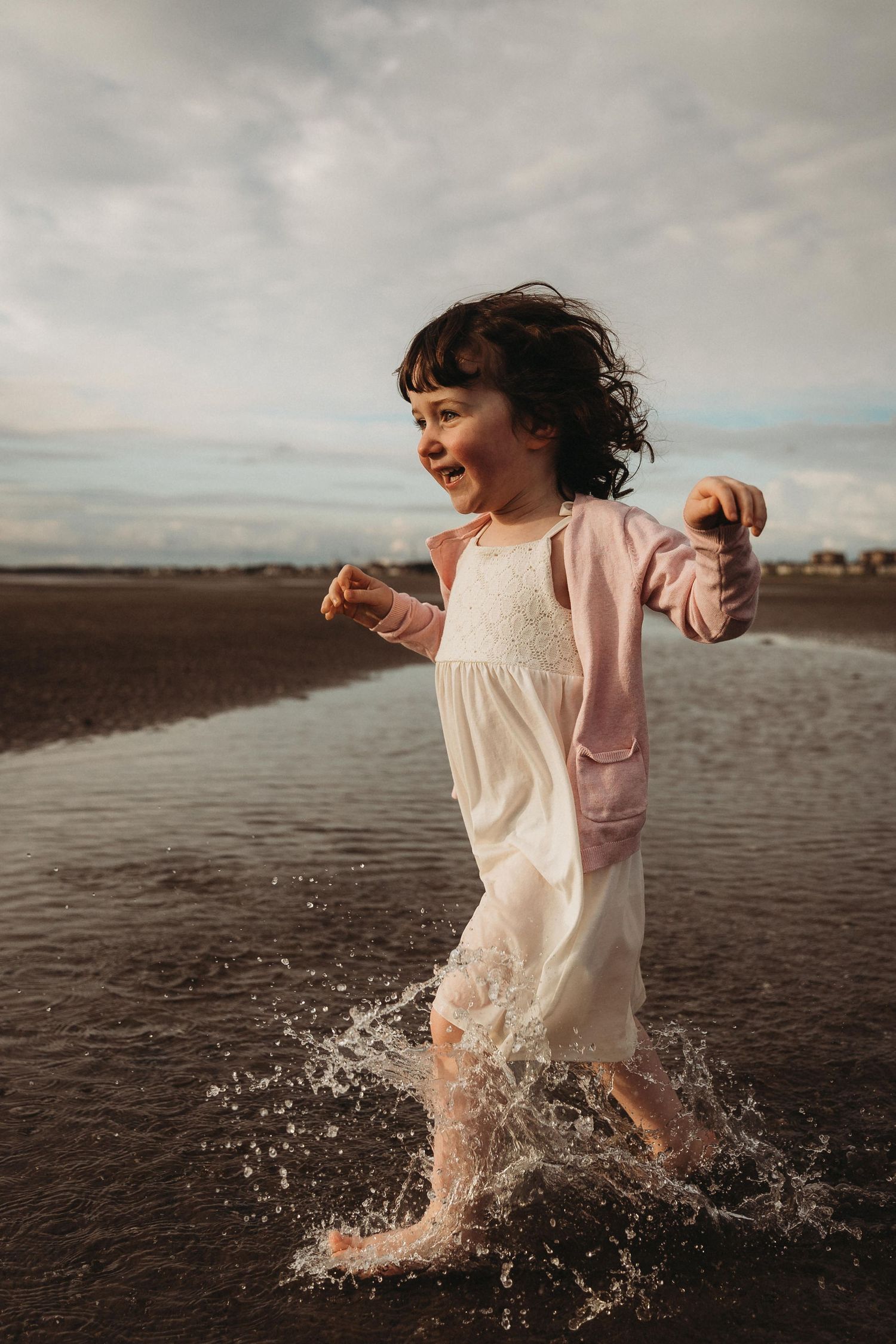 Young child running barefoot through shallow water at the beach, captured mid-movement