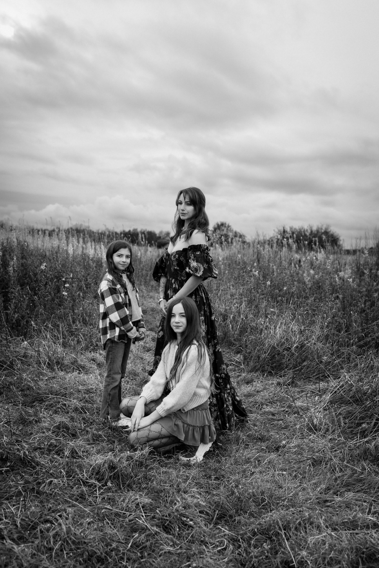 Black and white portrait of a mother posed with her three children in tall grass under an open sky