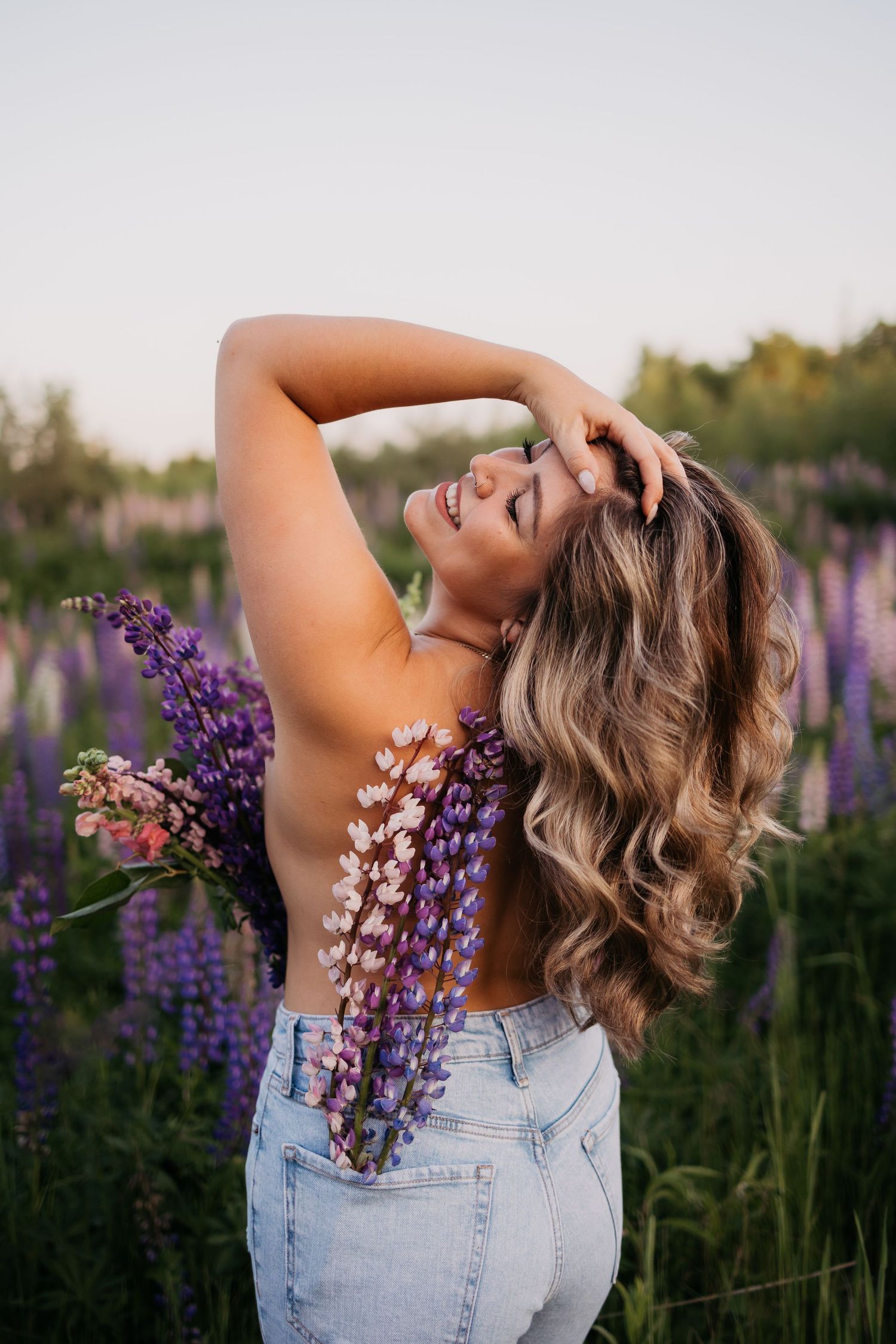 Woman posing joyfully in field of purple lupine flowers at golden hour.