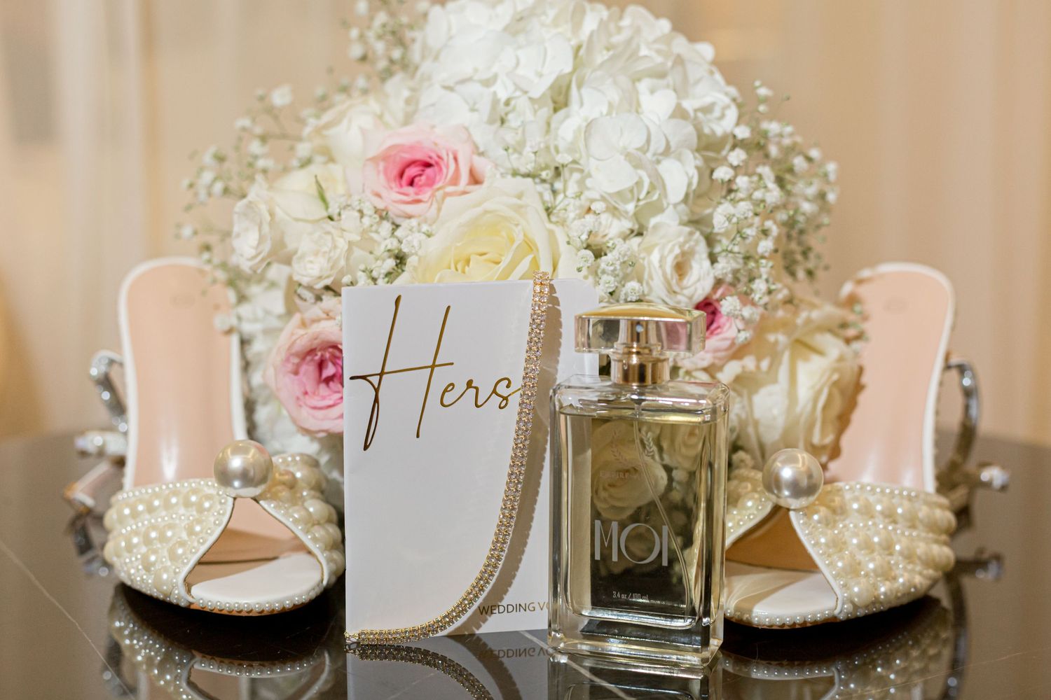 Wedding accessories with bridal shoes, perfume bottle and floral arrangement with pink roses and white hydrangeas.