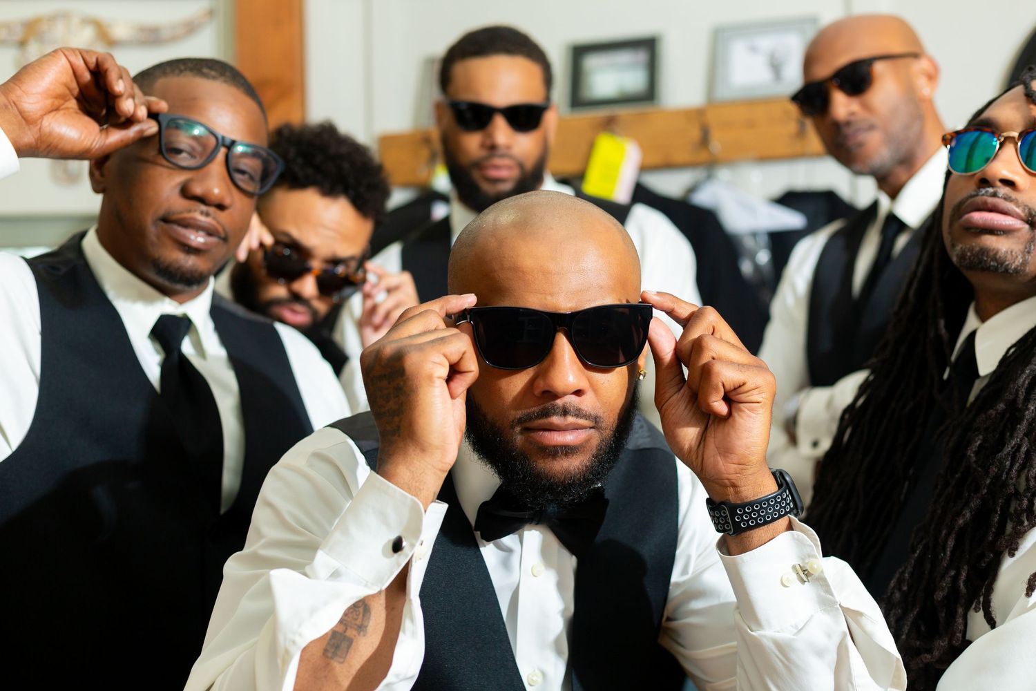 Groomsmen in black suits and sunglasses pose for a stylish wedding party photo.
