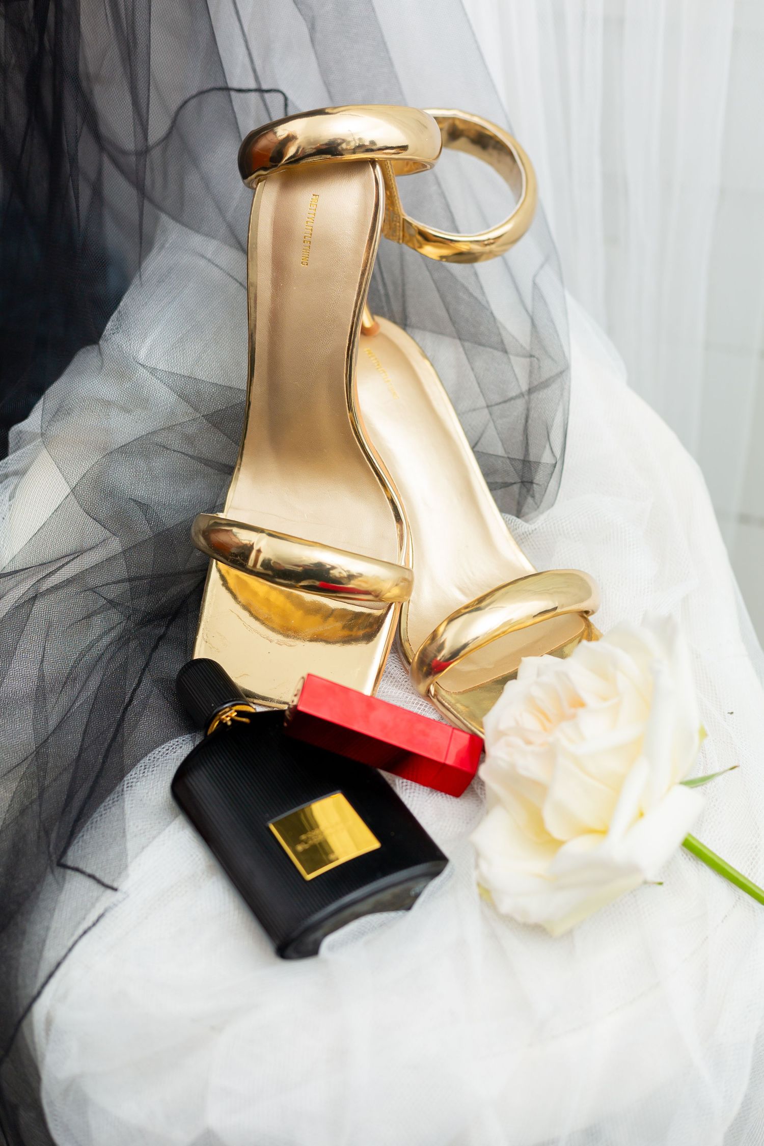 Gold wedding heels with lipstick and perfume styled on white tulle fabric.