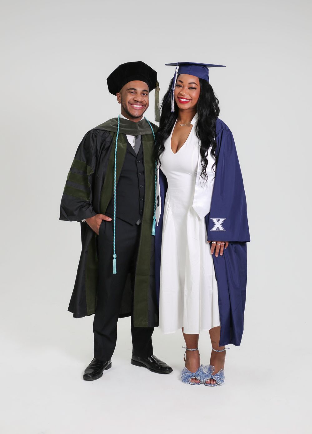 Two graduates in caps and gowns pose together, one in doctoral regalia and one in navy blue graduation attire.