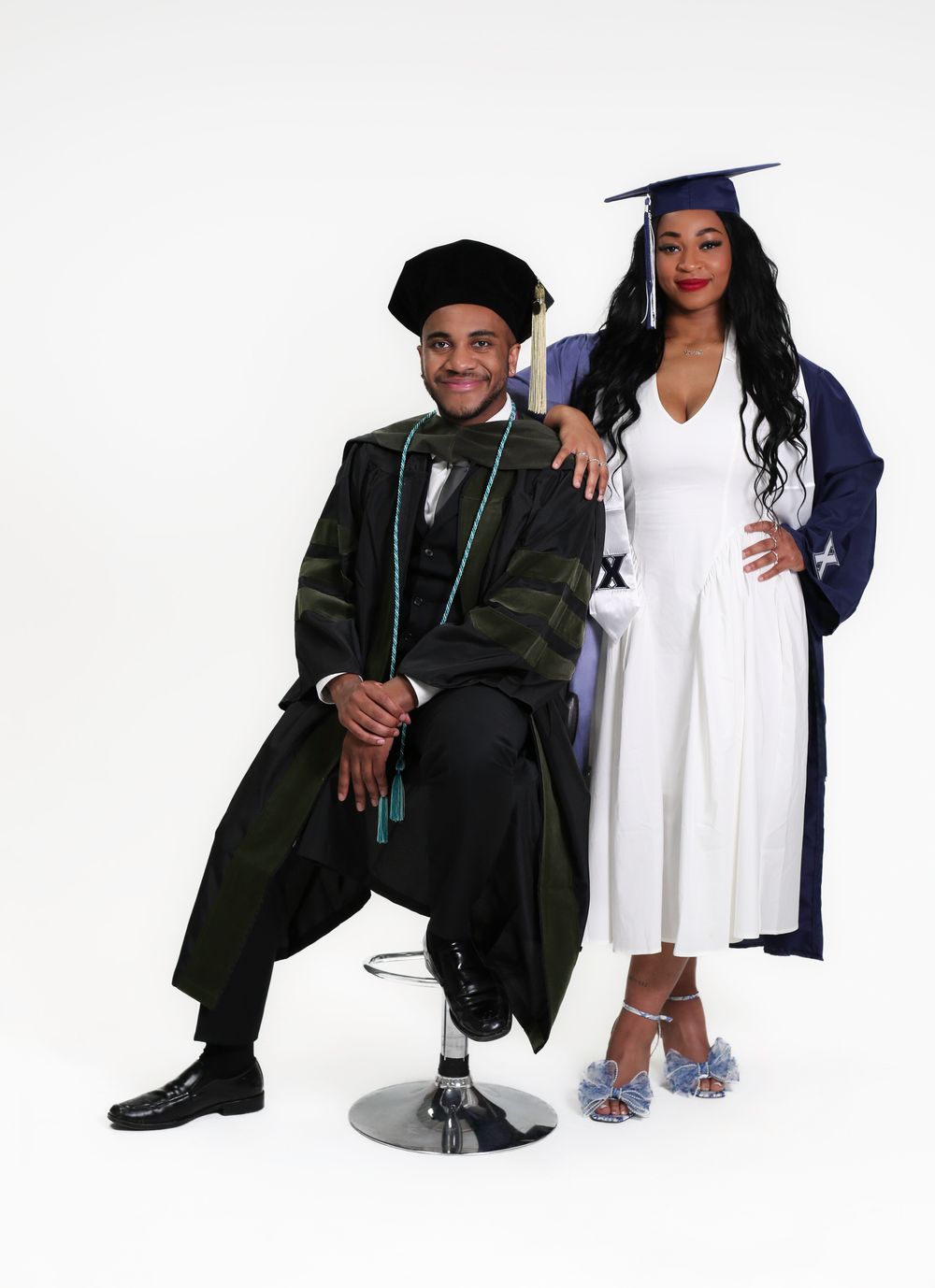 Two graduates in academic regalia pose together for a formal graduation portrait against a white background.
