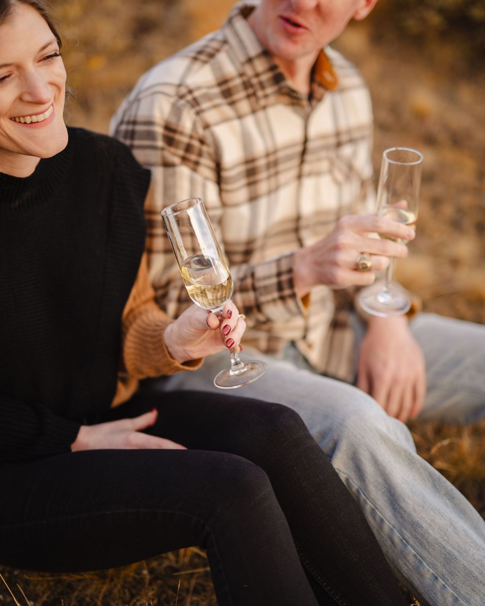 A couple sits together outdoors sharing champagne at golden hour.