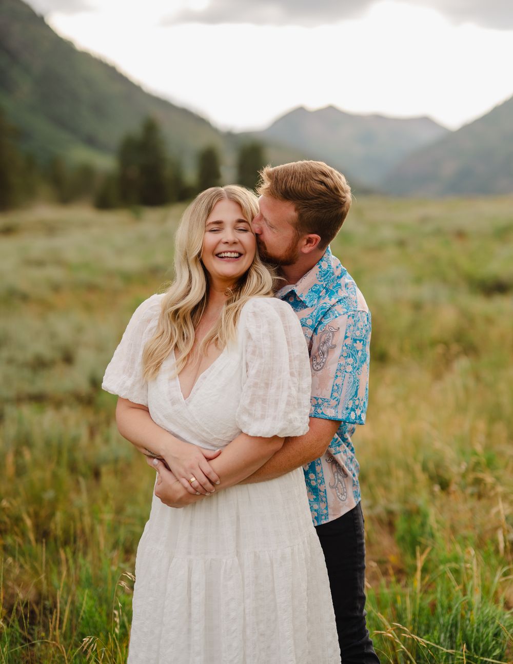 Joyful couple embracing in a mountain meadow during golden hour.