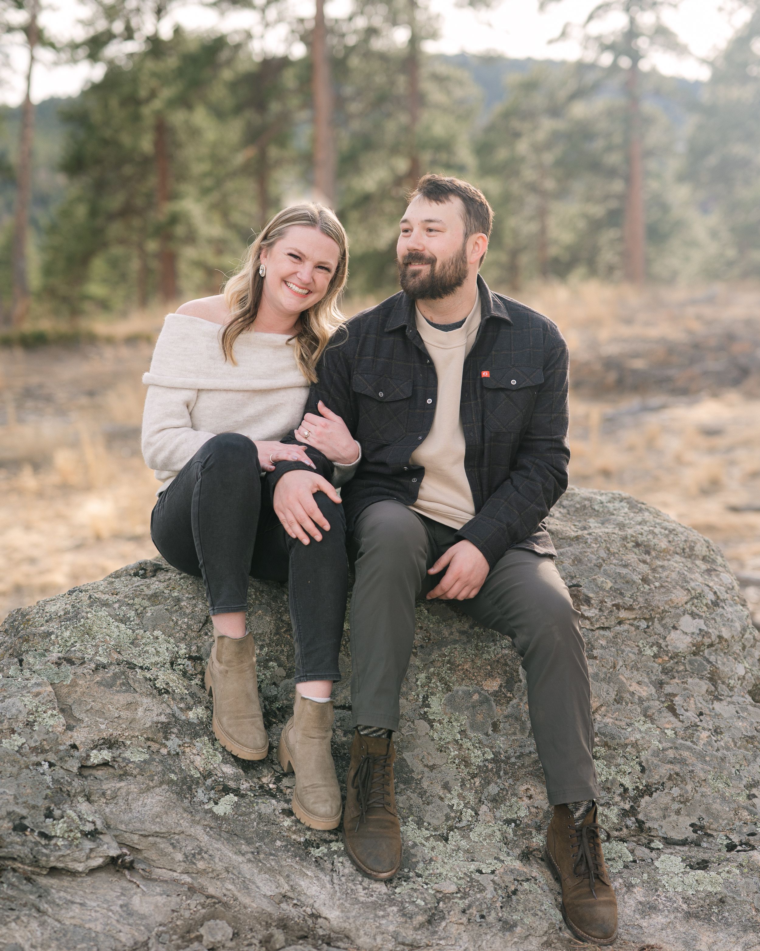 A couple sits together on a rocky outcrop in a scenic outdoor setting during golden hour.
