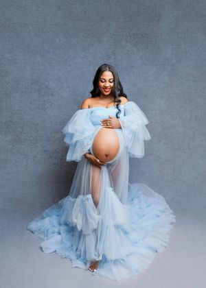 A maternity photo series showing a woman in a flowing light blue tulle gown against a gray backdrop.