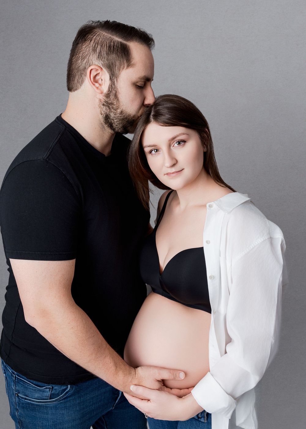 A pregnant couple in contrasting black and white outfits embrace during a minimalist maternity photoshoot.