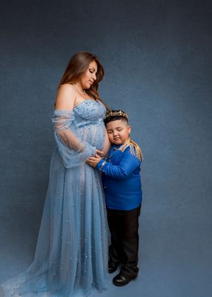 A tender moment captured in a maternity photo shoot with a child embracing a pregnant figure in a flowing blue gown.