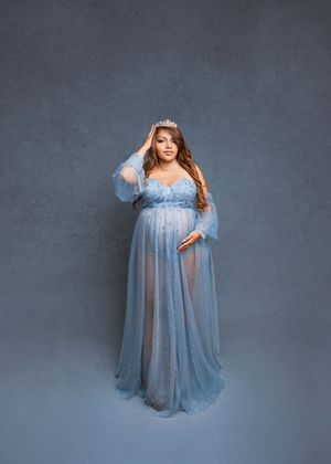 A maternity photoshoot featuring a flowing blue gown against a grey backdrop in multiple elegant poses.