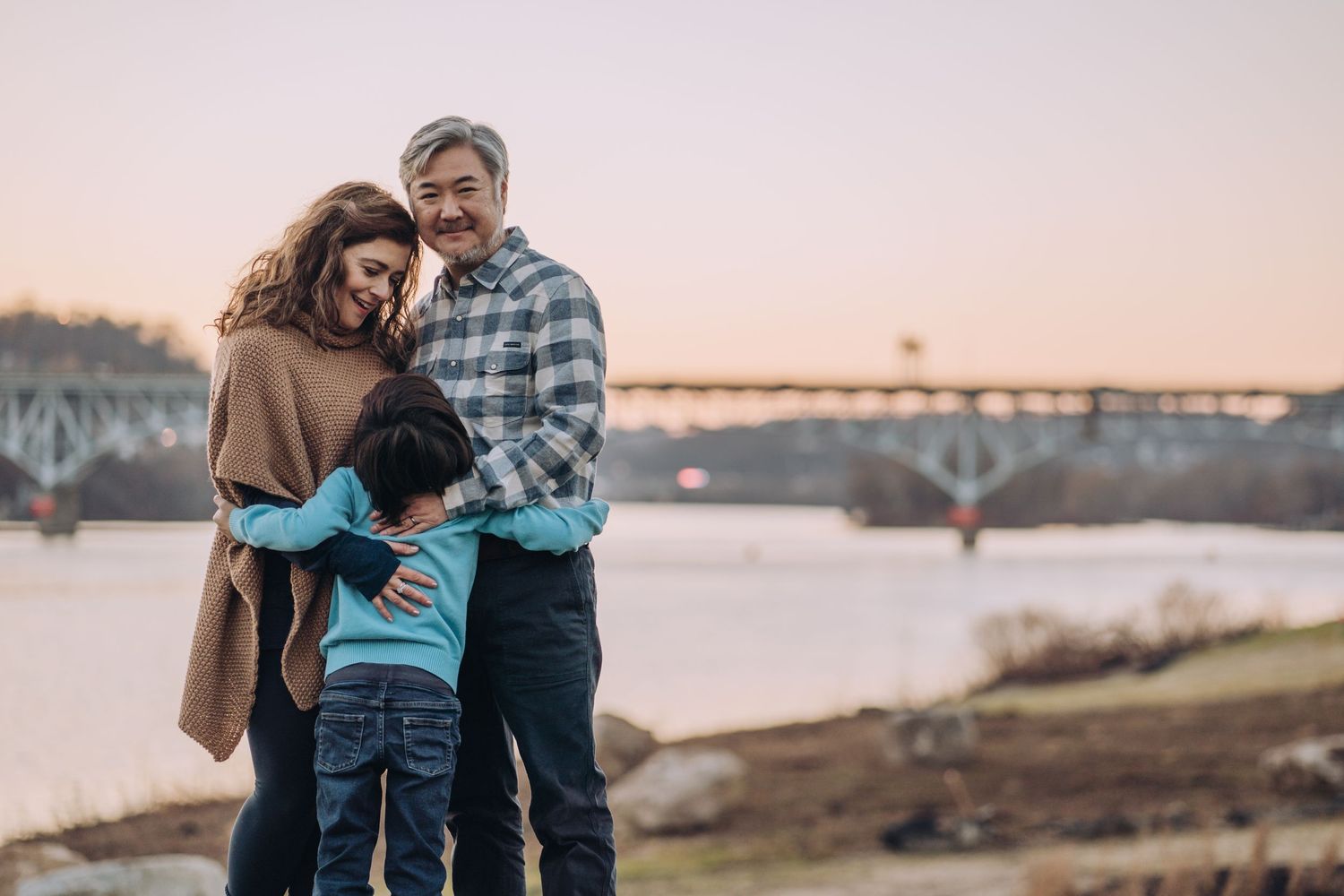 A family of three hugs with sunset and Pittsburgh bridges behind them. Shannon Konek, Pittsburgh Photographer