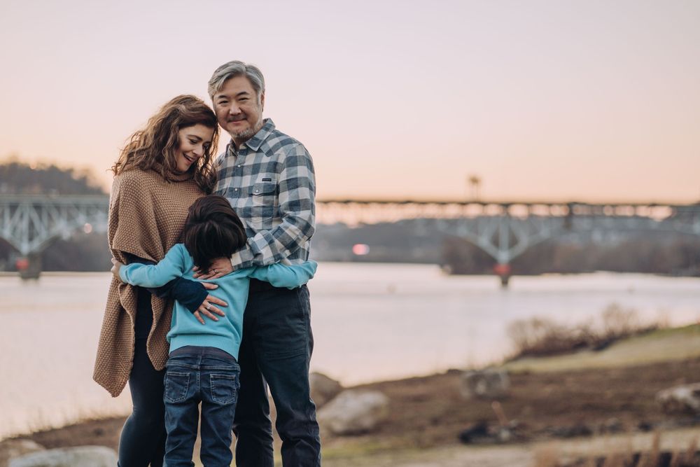 A family of three hugs with sunset and Pittsburgh bridges behind them. Shannon Konek, Pittsburgh Photographer