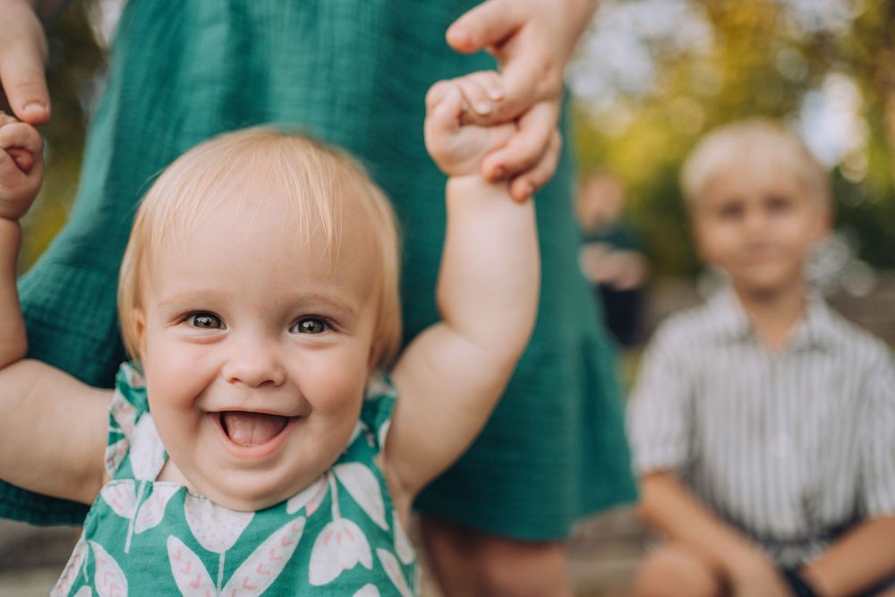 Close up of a baby's smiling face, as her sister holds the baby's hands. Shannon Konek, Pittsburgh Photographer