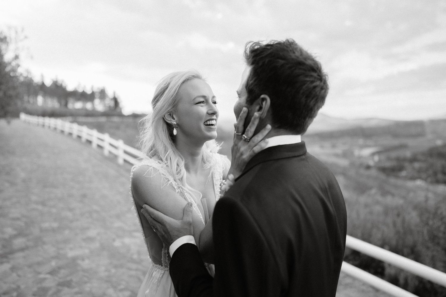 Black and white candid moment of newlyweds laughing together against countryside backdrop.