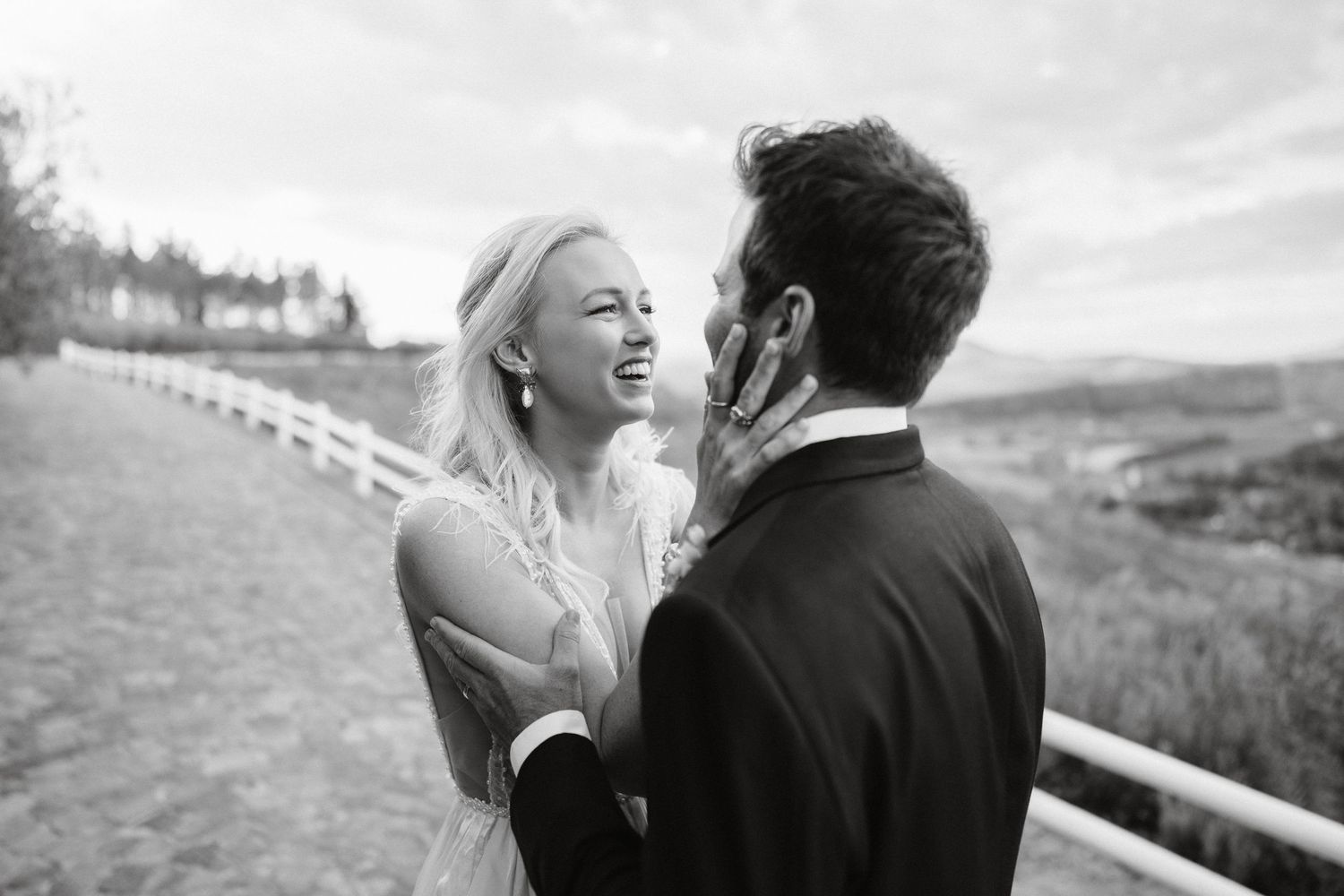 Black and white candid moment of newlyweds laughing together against countryside backdrop.