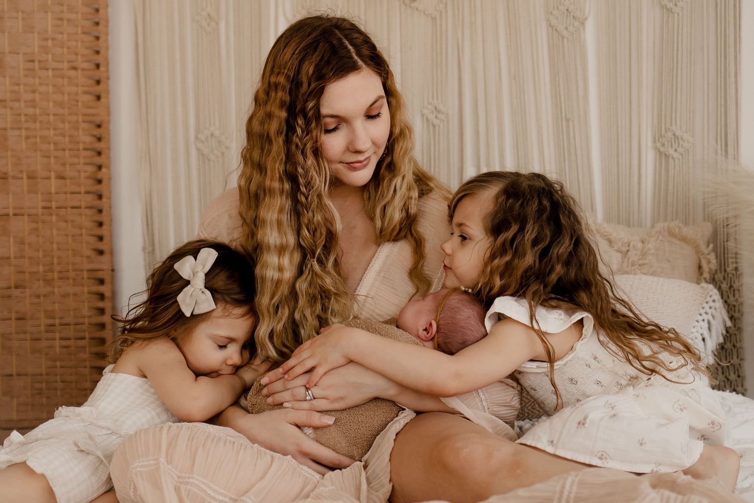 Mom with three little girls snuggle on the bed during a boho motherhood newborn session with Fully Known Services.
