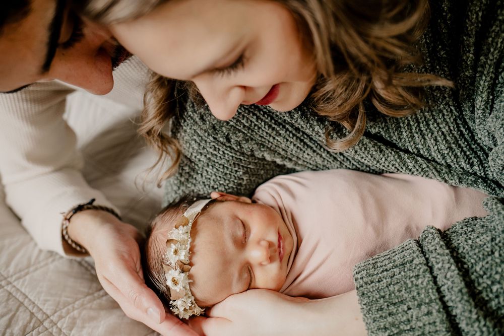 Newborn photography of newborn in her mothers arms on the bed with dad behind them. Photography captured in St. Charles County.