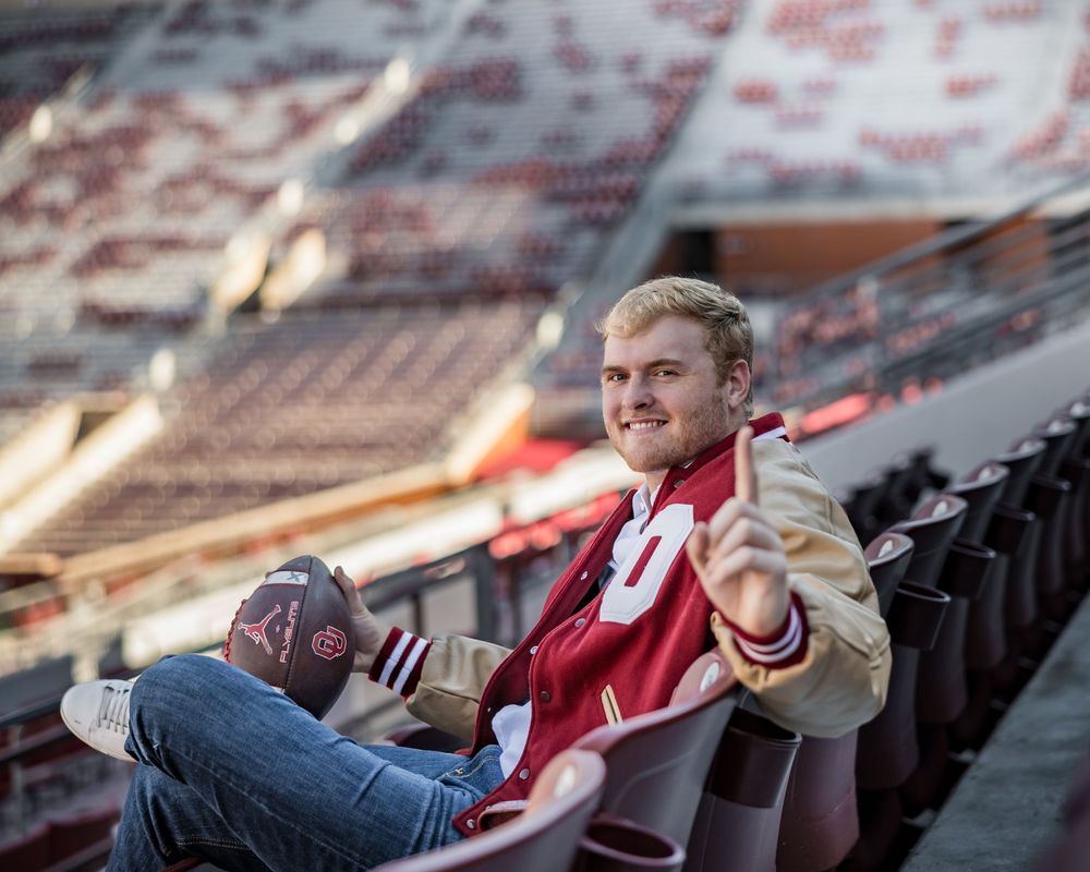 A person wearing a red sports jersey sits alone in empty stadium seats at sunset.