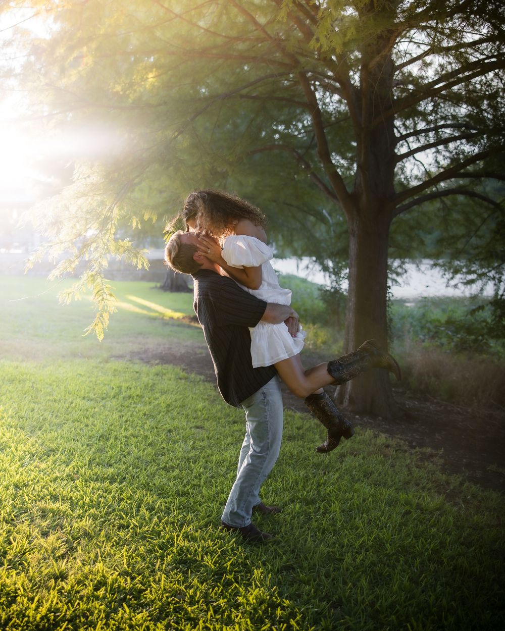 A couple dances in a sunlit meadow at sunset creating a romantic silhouette against the golden light.