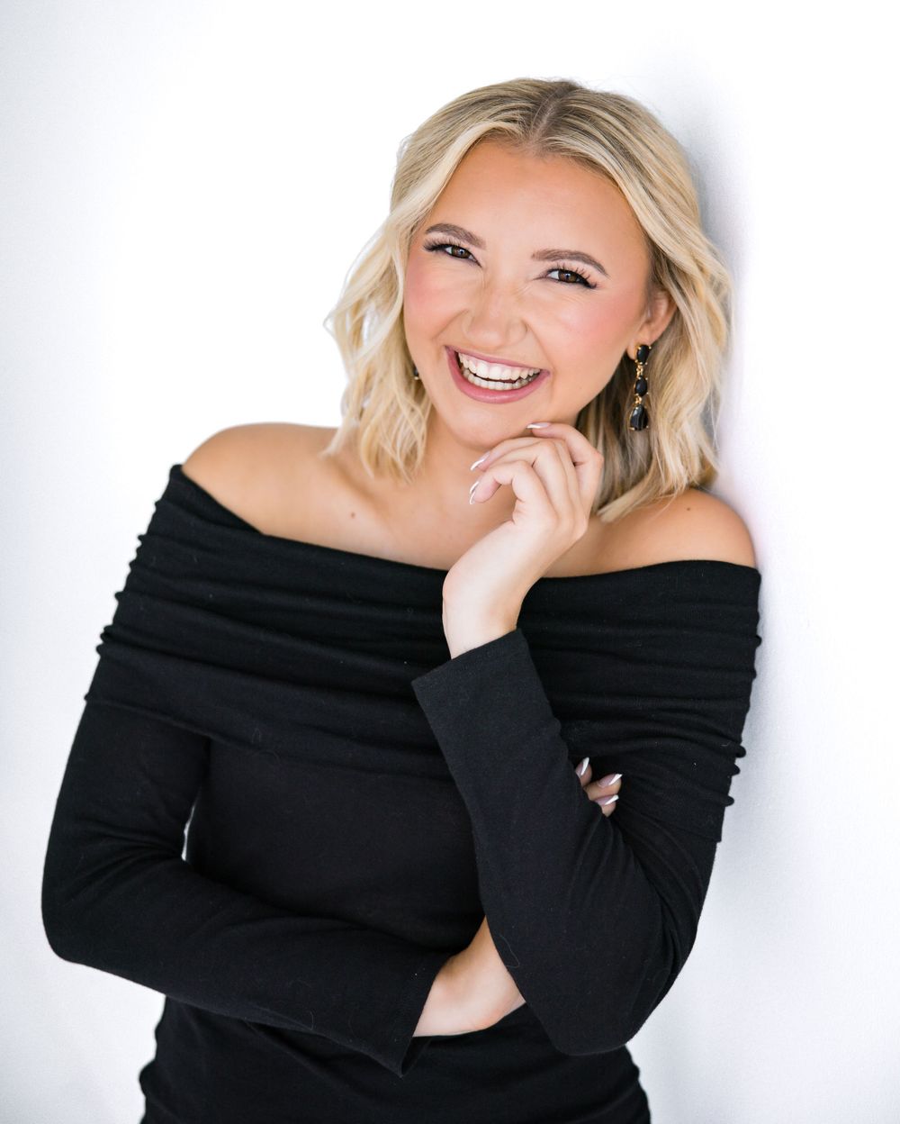 Studio portrait in black off-shoulder sweater against white background with natural smile.