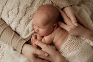 Peaceful newborn baby sleeping on soft white knitted blankets while being cradled by gentle hands.